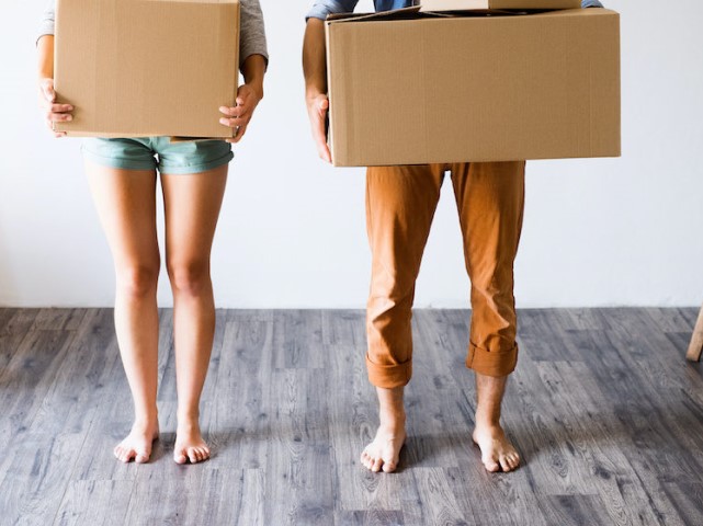 Unrecognizable young married couple moving in new house, holding big cardboard boxes.