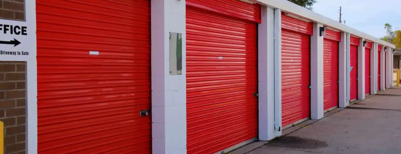 Row of outdoor self-storage units with bright red roll-up doors and white concrete block walls